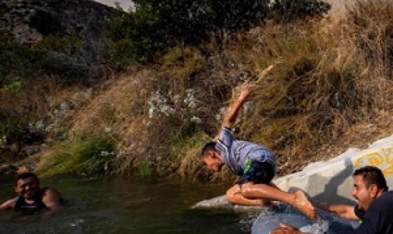 Eddie Lopez and his son, Eddie Jr. frolic near a drainage pipe along the San Gabriel River, in California, during the recent heat wave.  PHOTOGRAPH BY ROBERT GAUTHIER, LOS ANGELES TIMES/GETTY IMAGES
